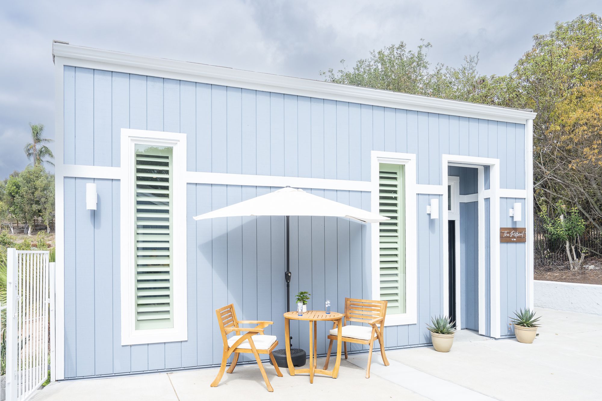 Rancho Bernardo garage converted into a blue board-and-batten ADU with green shutters, a patio set and an umbrella