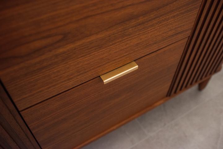 Walnut drawer front with a slim brass pull, fluted panel and tapered leg alongside