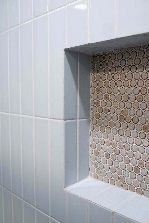 Recessed niche lined in penny round mosaic, framed by pale blue stacked tile