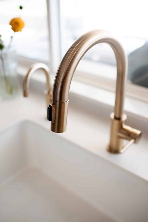 Two champagne bronze faucets at the white farmhouse sink