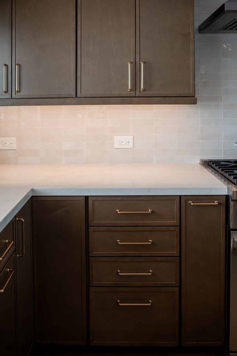 Warm brown shaker cabinets with brass bar pulls, quartz counter, and under-cabinet lighting