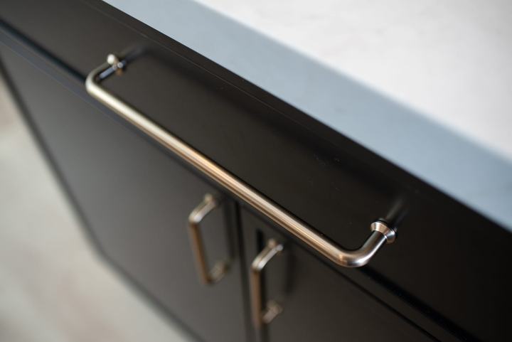 Close-up of a brass bar pull on the black island cabinetry