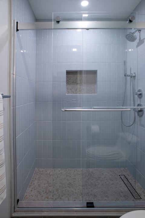 Shower in its own compartment, pale blue vertical tile and a penny round mosaic floor