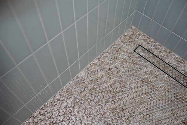 Corner of the shower where the vertical wall tile meets the penny round floor and drain