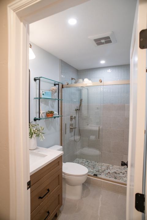 The bathroom seen through its doorway: vanity, toilet, and tiled shower with a pebble floor