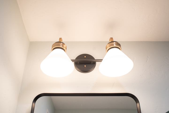 Two-light vanity fixture with cone shades in bronze and brass above the mirror frame