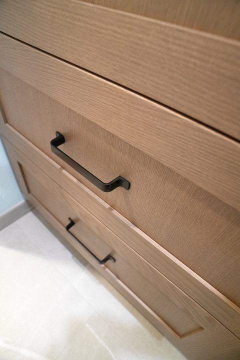 Matte black pulls on the straight-grained wood drawers of the vanity
