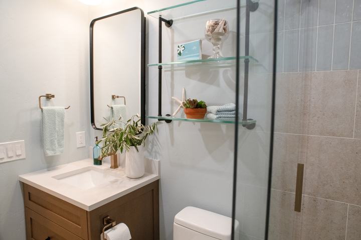 Vanity, towel ring, and styled glass shelves seen past the edge of the sliding shower door