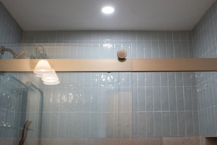 Bronze track and round roller of the Kohler Levity sliding door against glossy blue tile