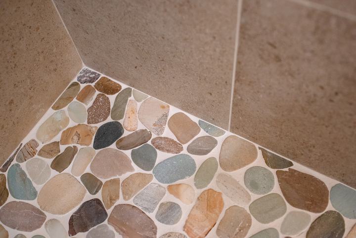 Corner where the Waterbrook sliced pebble shower pan meets the speckled beige wall tile
