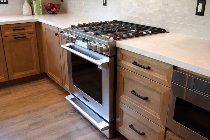 Gas range seen at an angle with maple cabinetry and drawer fronts alongside