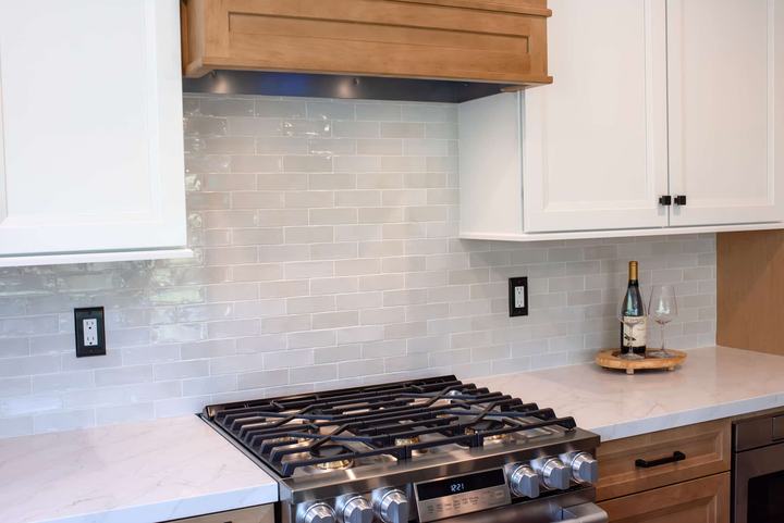Gloss backsplash tile meeting white uppers at the range, wine glasses on the counter