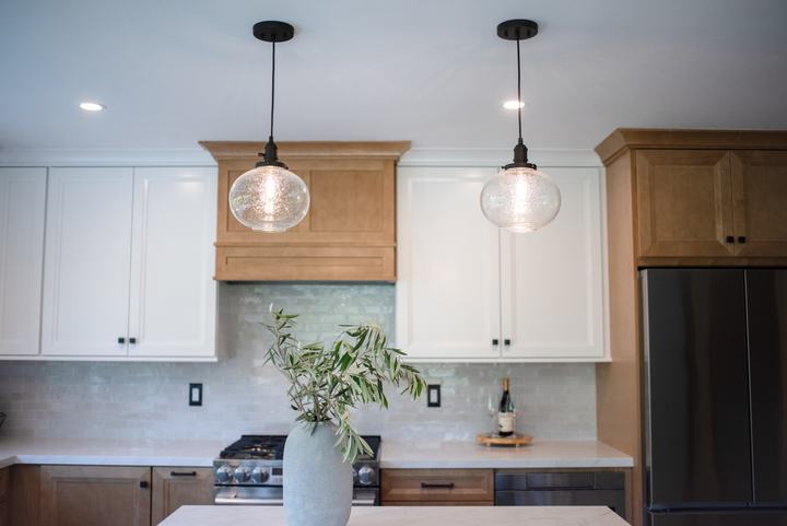Two seeded glass pendants in front of the wood hood surround and white upper cabinets
