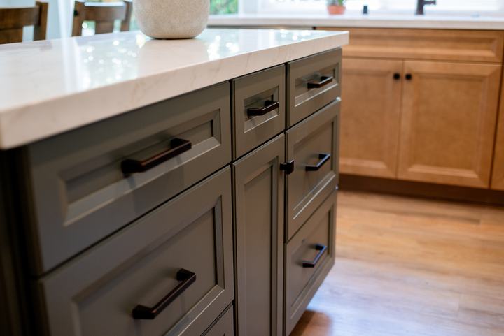 Bronze pulls across the green island fronts with maple cabinetry behind