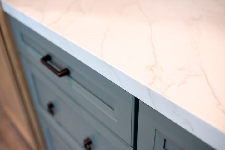 Quartz countertop edge meeting the green island drawer fronts and bronze pull