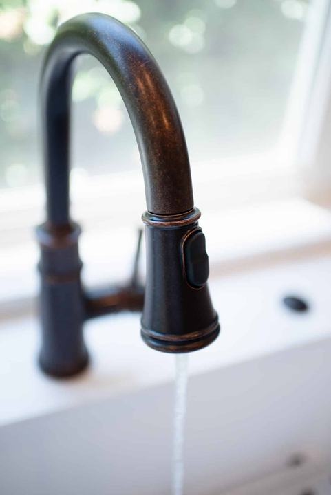 Oil-rubbed bronze pull-down faucet running water into the sink below the window