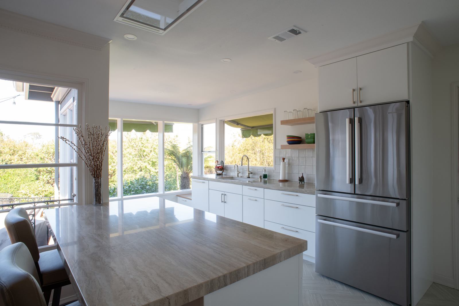 Porcelain-topped island in front of white cabinetry, a French door refrigerator, and a wall of windows
