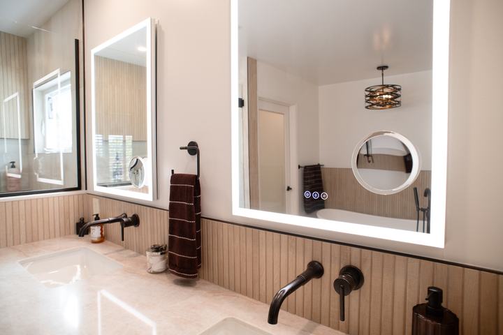 Lighted mirror reflecting the tub and chandelier across the room