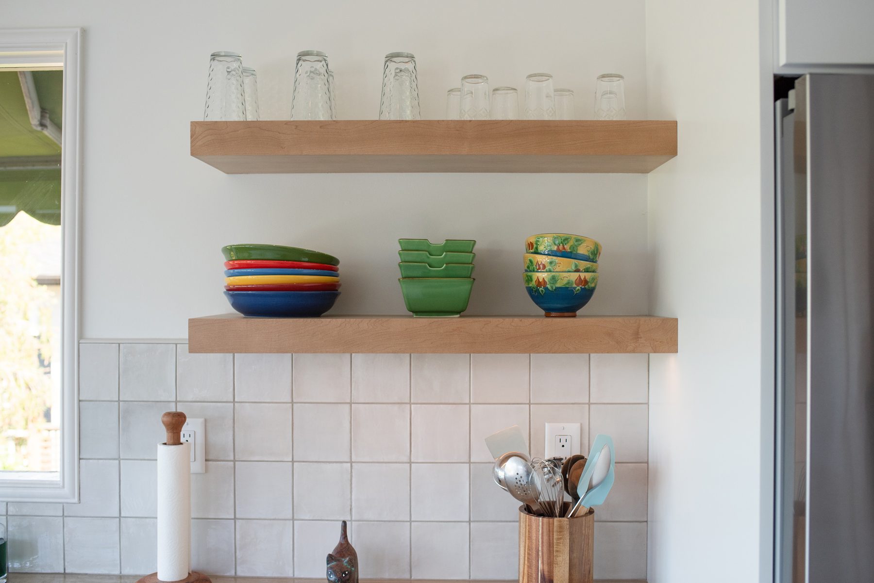 Wood floating shelves holding everyday dishes above a white tile backsplash in a Point Loma kitchen