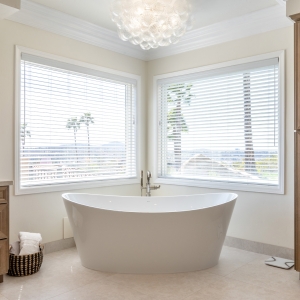 Corner BainUltra tub framed by picture windows with hillside view and bubble chandelier above