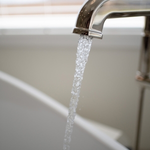 Detail of curved polished-nickel tub spout with streaming water into white freestanding tub