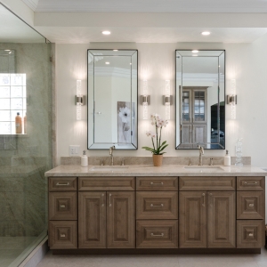 Double-sink vanity with beveled mirrors beside frameless glass shower clad in Taj Mahal quartzite