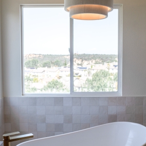 Freestanding tub beneath modern pendant, framed by panoramic window.