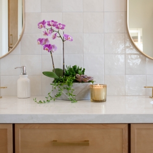 Orchid centerpiece on quartz countertop between twin brushed-gold faucets.