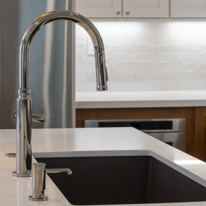 Close-up of chrome pull-down faucet over composite sink set in quartz island; subway backsplash behind