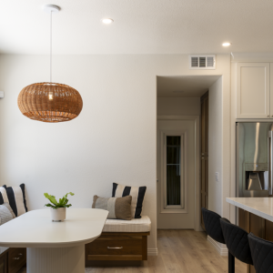 Window banquette with striped pillows, fluted pedestal table, woven rattan light, and glimpse of fridge