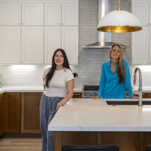 Two Kaminskiy designers standing behind quartz island in completed Poway two-tone kitchen remodel