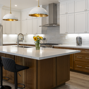 Wide view of Poway kitchen remodel with quartz-top walnut island, white shaker uppers, brass dome pendants, and wood floors