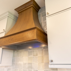 Detail of custom stained wood range hood framed by Painted Harbor uppers and handcrafted ceramic tile