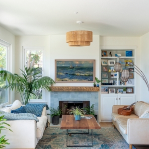 Adjacent family room with coastal fireplace surround, built-ins, woven pendant, and layered blue accents