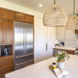 Built-in French-door refrigerator and coffee niche beside island with quartz top and woven pendants in a warm cherry and paint palette