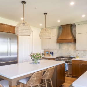 Island seating with woven stools and pendants facing custom wood hood and two-tone cabinetry