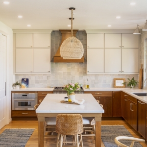 Centered view of two-tone kitchen with large island seating, custom wood hood, zellige-style Marin tile backsplash, and soft recessed lighting