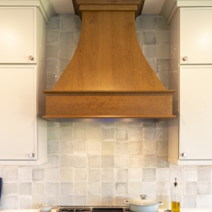 Centered view of custom stained wood hood with glossy Marin ceramic tile backsplash and Painted Harbor uppers