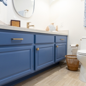 Blue cabinet vanity with brass pulls beside the toilet; light quartz countertop