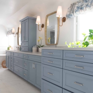 Long blue double-sink vanity with gold sconces, woven-frame mirrors, and quartz countertop