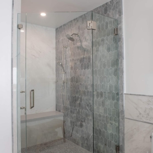 Corner shower with frameless glass panels, blue-gray lotus tile wall, and penny round shower floor