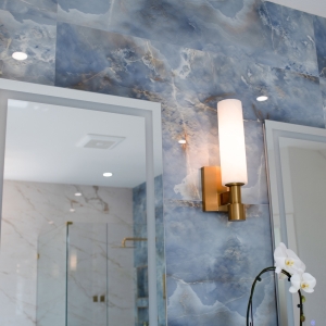 Brass wall sconces beside illuminated mirrors on a blue onyx-look tile feature wall