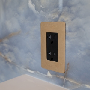 Close-up of a black outlet with a brass faceplate on blue onyx-look tile