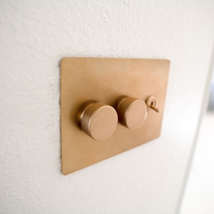 Brass wall plate with two dimmer knobs and a toggle switch on a white wall