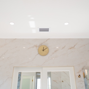 Brass wall clock above marble-look wall tile with recessed ceiling lights