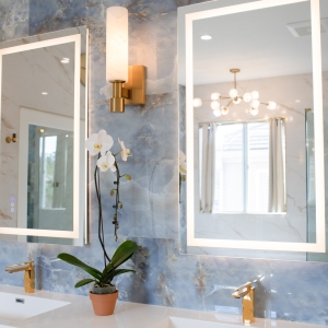 Front view of double vanity with illuminated mirrors and brass sconces on blue tile