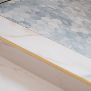 Close-up of shower curb with brass edge and blue hex mosaic tile flooring
