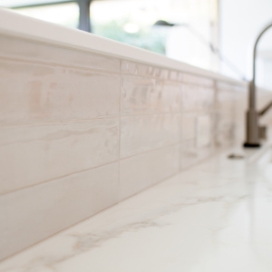 Glossy porcelain backsplash and kitchen faucet detail in remodeled kitchen